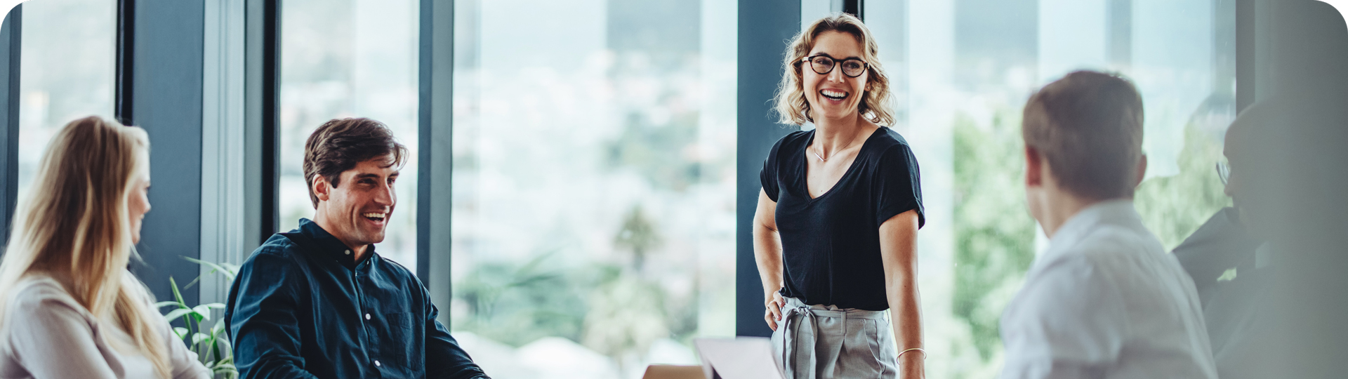 Vier Mitarbeitende sitzen und stehen lachend in einem modernen, lichtdurchfluteten Büro während eine Frau eine Präsentation hält – TASys