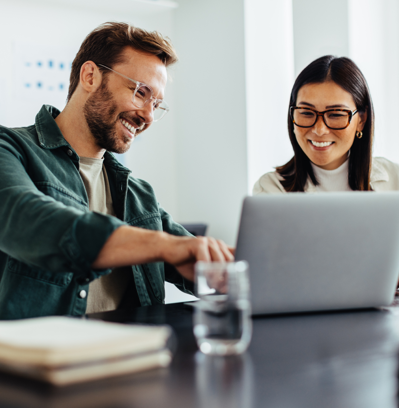 Zwei Mitarbeitende arbeiten lachend gemeinsam an einem Laptop in einem modernen Büro – TASys
