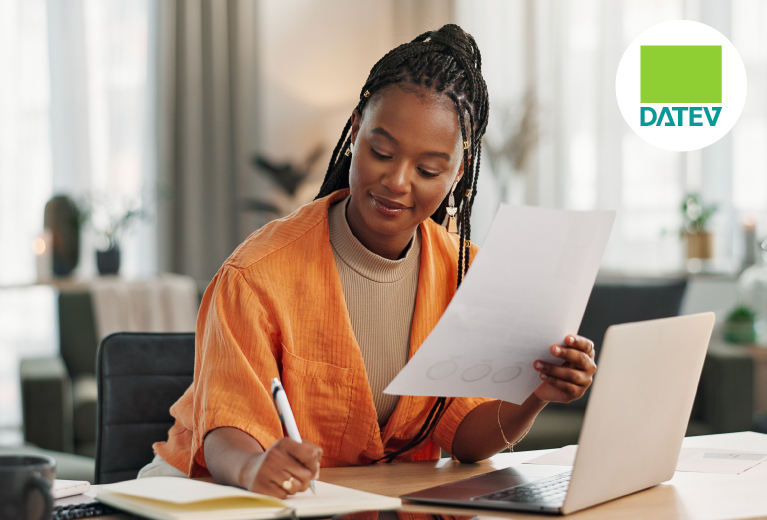 Frau prüft Unterlagen und schreibt Notizen am Laptop im Büro mit DATEV-Logo im Hintergrund – TASys