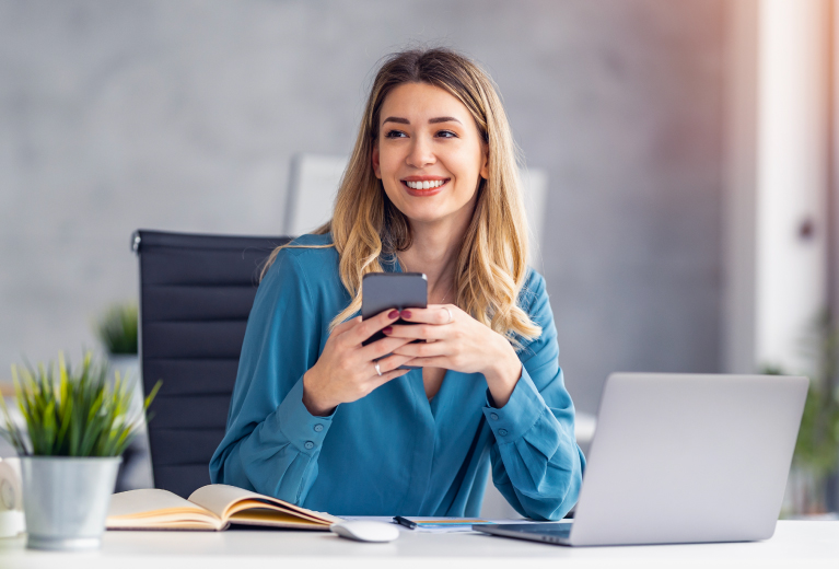 Frau arbeitet im Büro mit Smartphone und Laptop als Symbol für kaufmännische Qualifizierungen – TASys