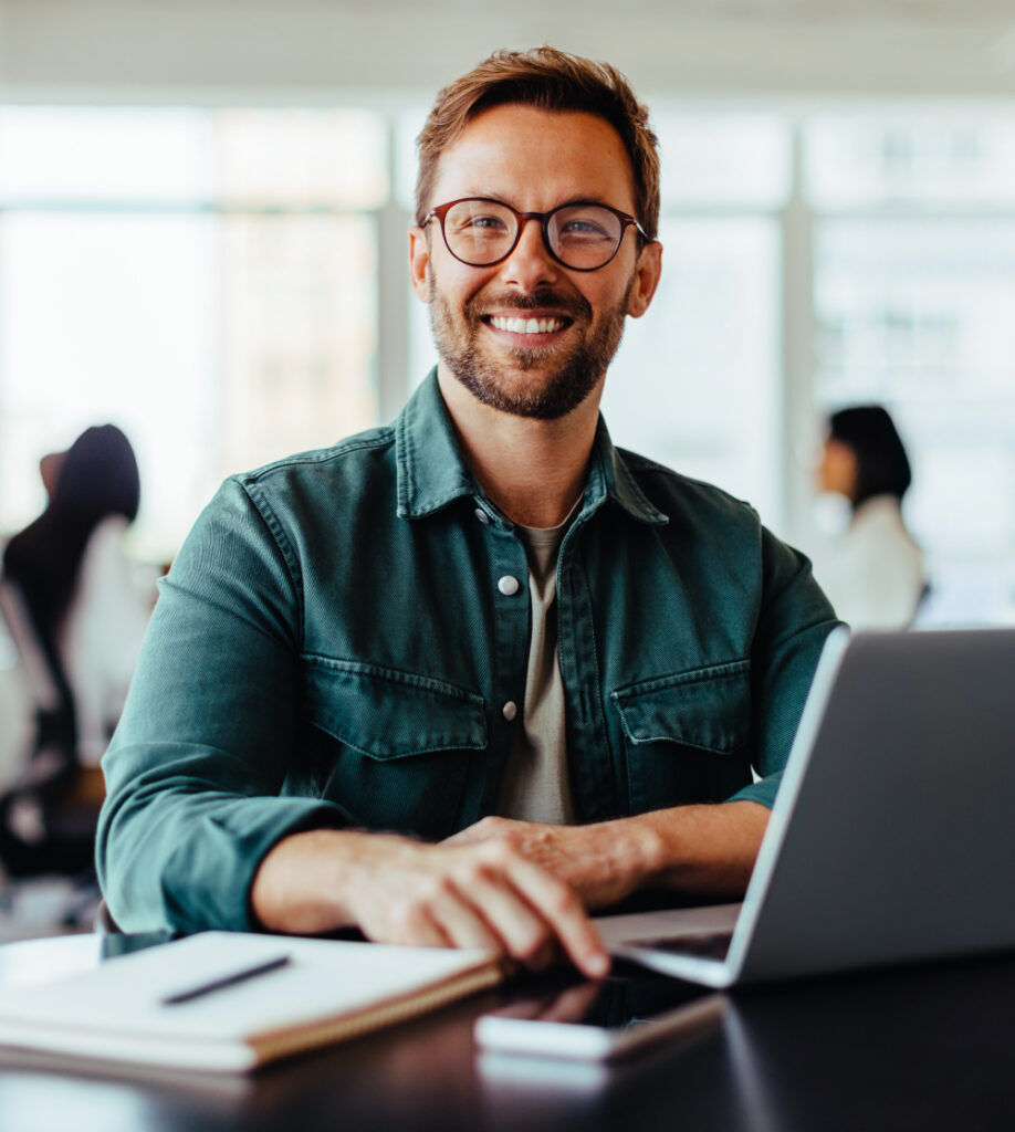 Mann arbeitet lächelnd am Laptop im modernen Büro als Symbol für SAP Kursübersicht bei TASys – TASys