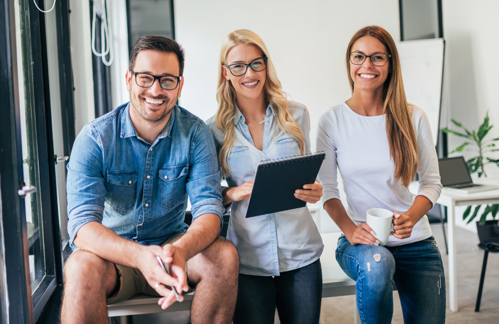 Drei lächelnde Mitarbeitende mit Tablet im modernen Büro als Symbol für das TASys Team – TASys