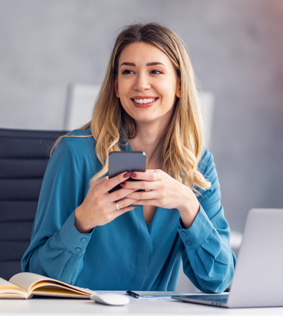 Frau mit Smartphone und Laptop im Büro als Symbol für kaufmännische Qualifikationen Kursübersicht bei TASys – TASys