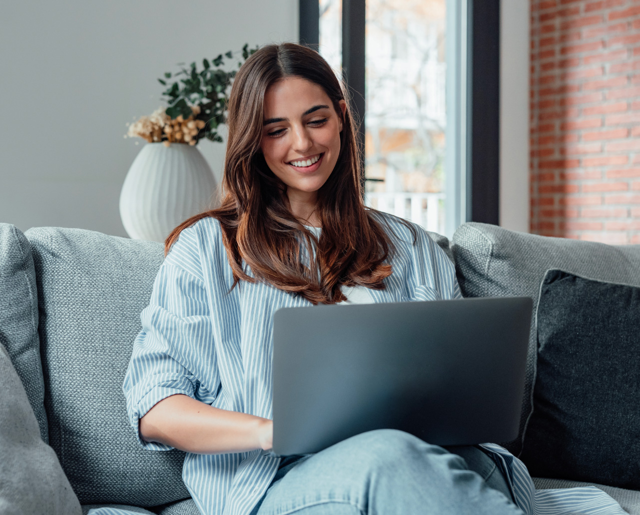 Junge Frau lernt entspannt zu Hause auf dem Sofa mit Laptop im Rahmen einer digitalen Weiterbildung – TASys