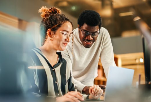 Zwei Personen arbeiten gemeinsam kreativ am Laptop im modernen Büro für eine Multimedia Weiterbildung – TASys